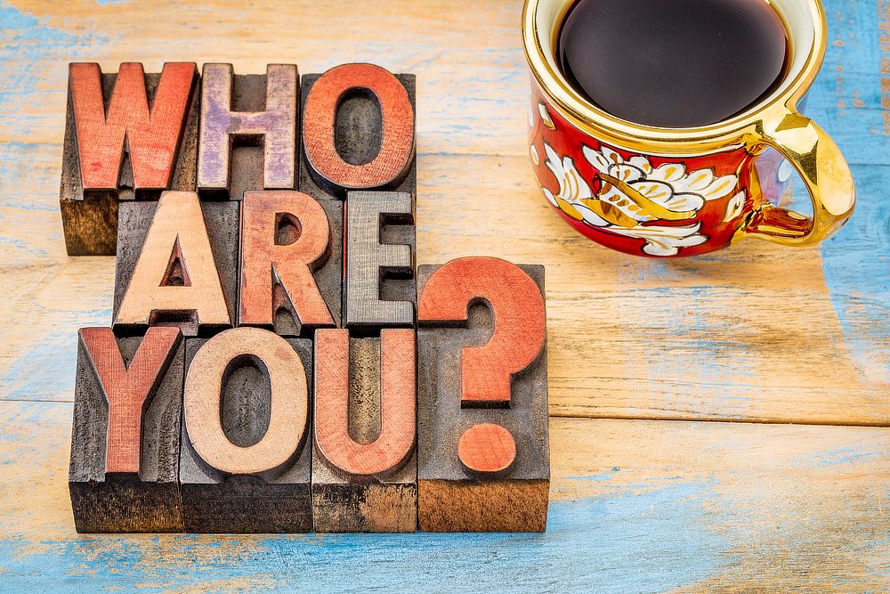 who are you question - word abstract in letterpress wood type blocks against grunge painted wood with a cup of coffee